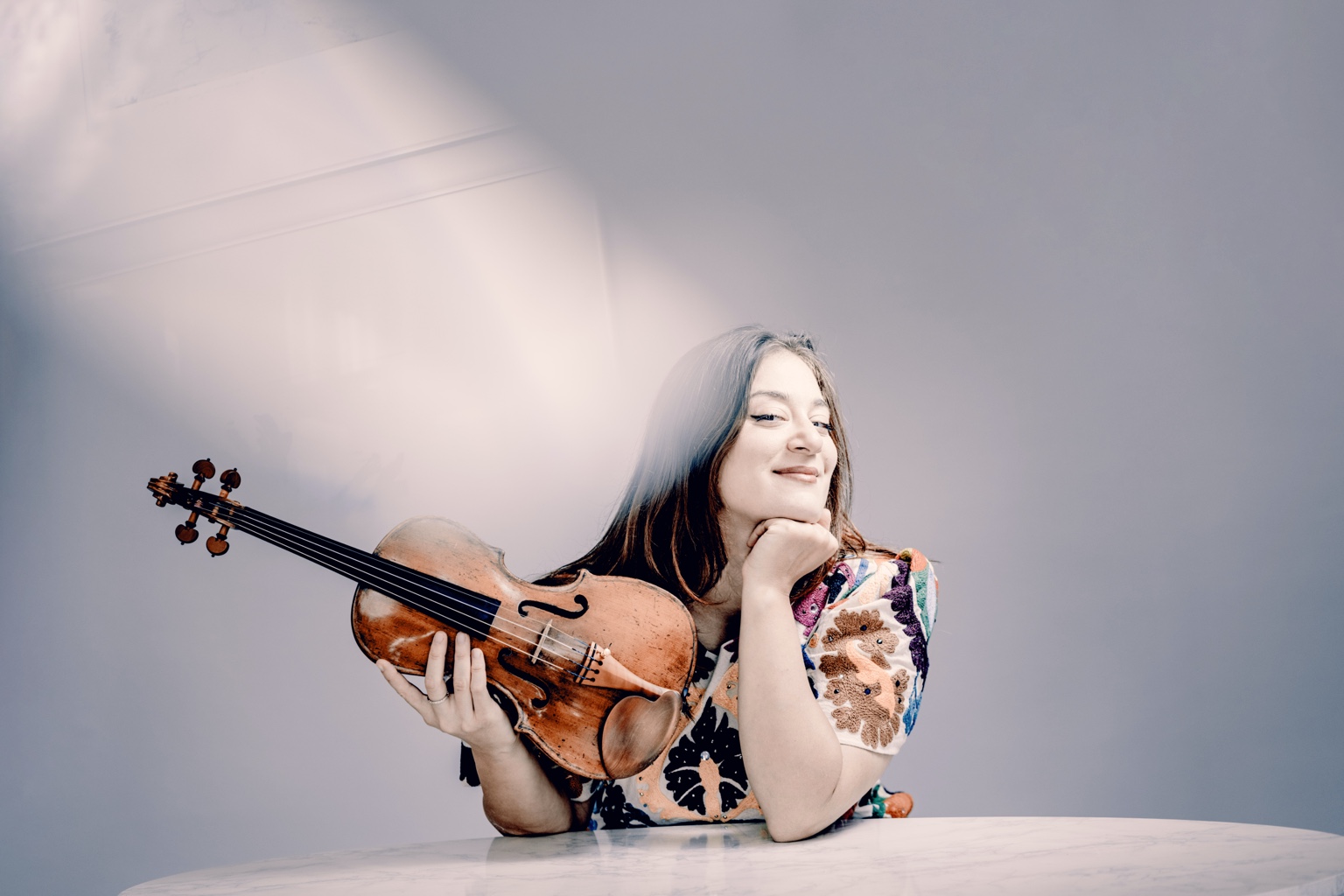 Veriko holding her violin at a table, photographed by Andrej Grilc